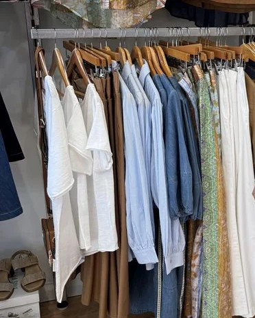 Inside the shop: linen shirts, denim and printed pants on the rail, a jacket and bags above
